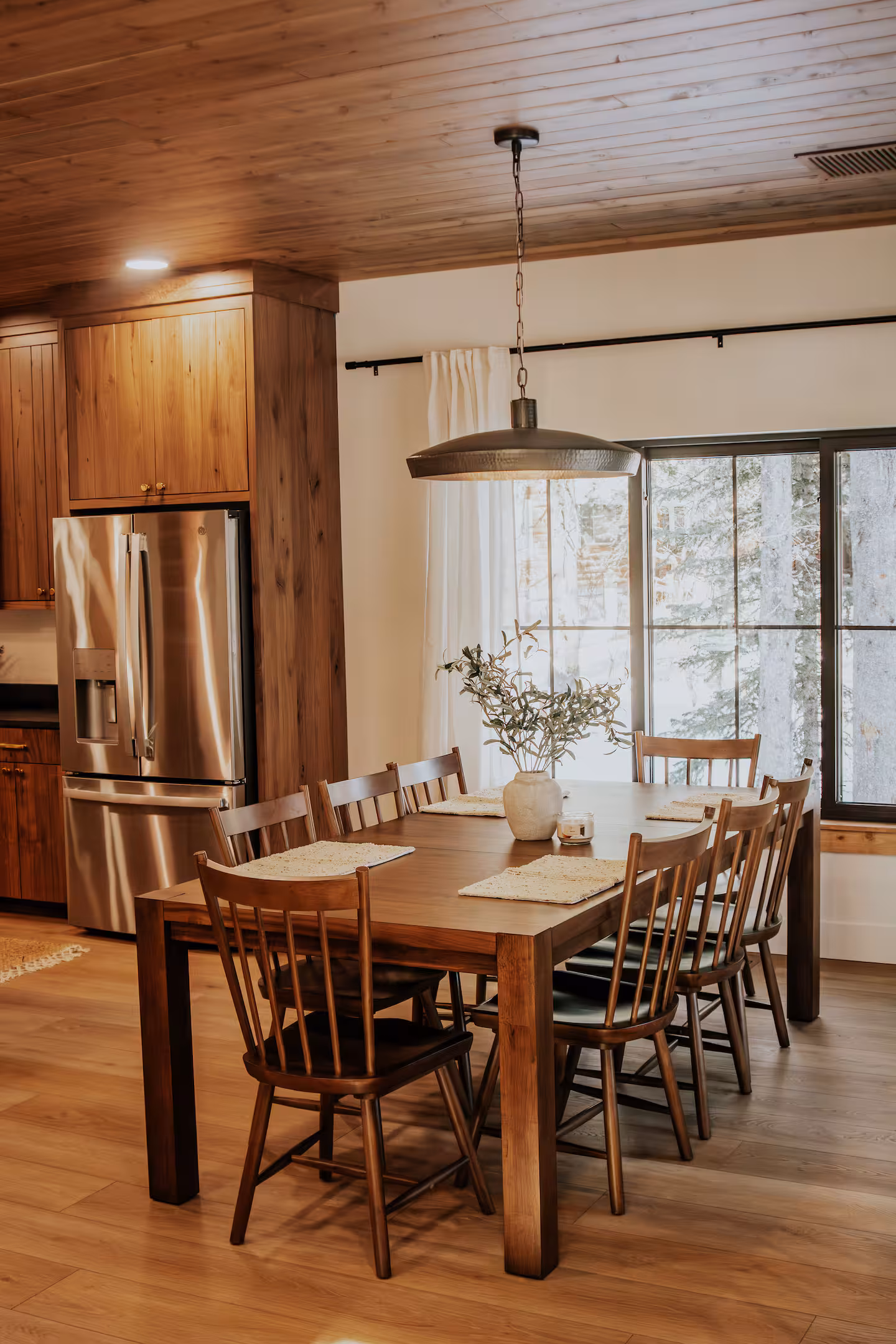 Walnut dining table under a black pendant with forest windows